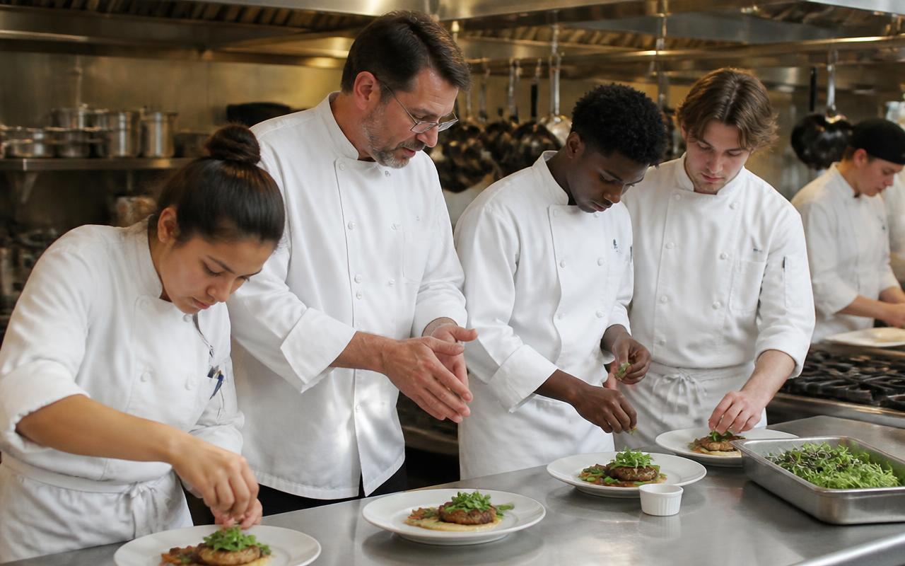 A culinary student plating dishes in a commercial teaching kitchen